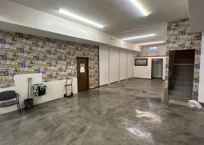A spacious, well-lit room with concrete flooring and colorful patterned wallpaper, featuring a door, chair, and stairs in the background.