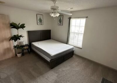 Cozy basement space featuring two recliners, a desk with a computer, and a lamp, all complemented by neat carpeting and bright windows.