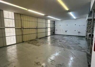 Spacious, empty garage with concrete flooring, large windows, and bright overhead lighting, ready for use or storage.